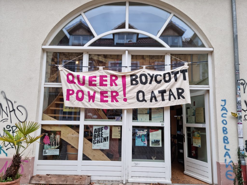 Eingangsbereich der Rosa Hilfe von außen, Über der Tür ist ein großes Banner angebracht mit der Schrift: QUEER POWER! BOYCOTT QATAR