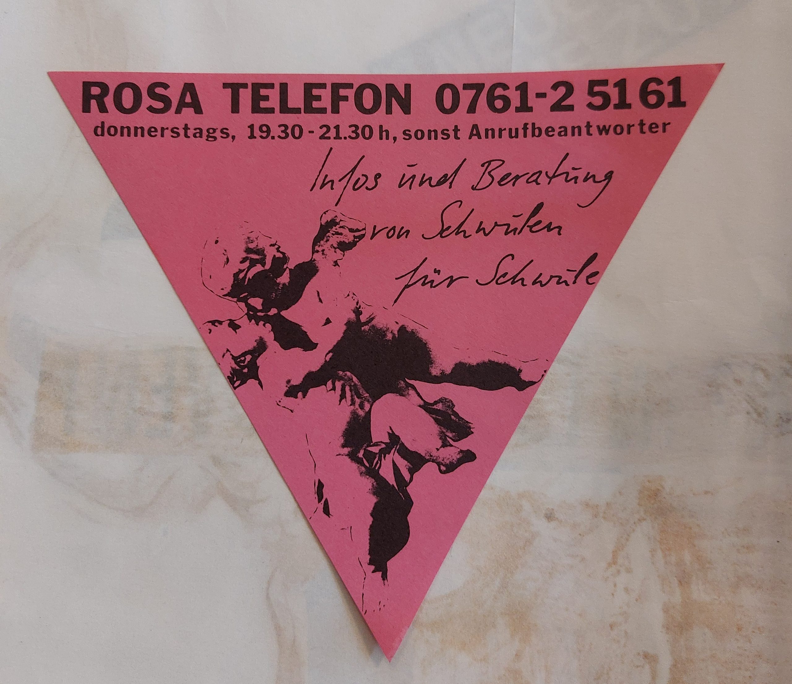 Flyer des Rosa Telefons in Form eines auf die Spitze gestellten Dreiecks, Pinkes papier, Text: ROSA TELEFON 0761-2 5161 Infos und Beratung von Schwulen für Schwule donnerstags, 19.30 - 21.30 h, sonst Anrufbeantworter