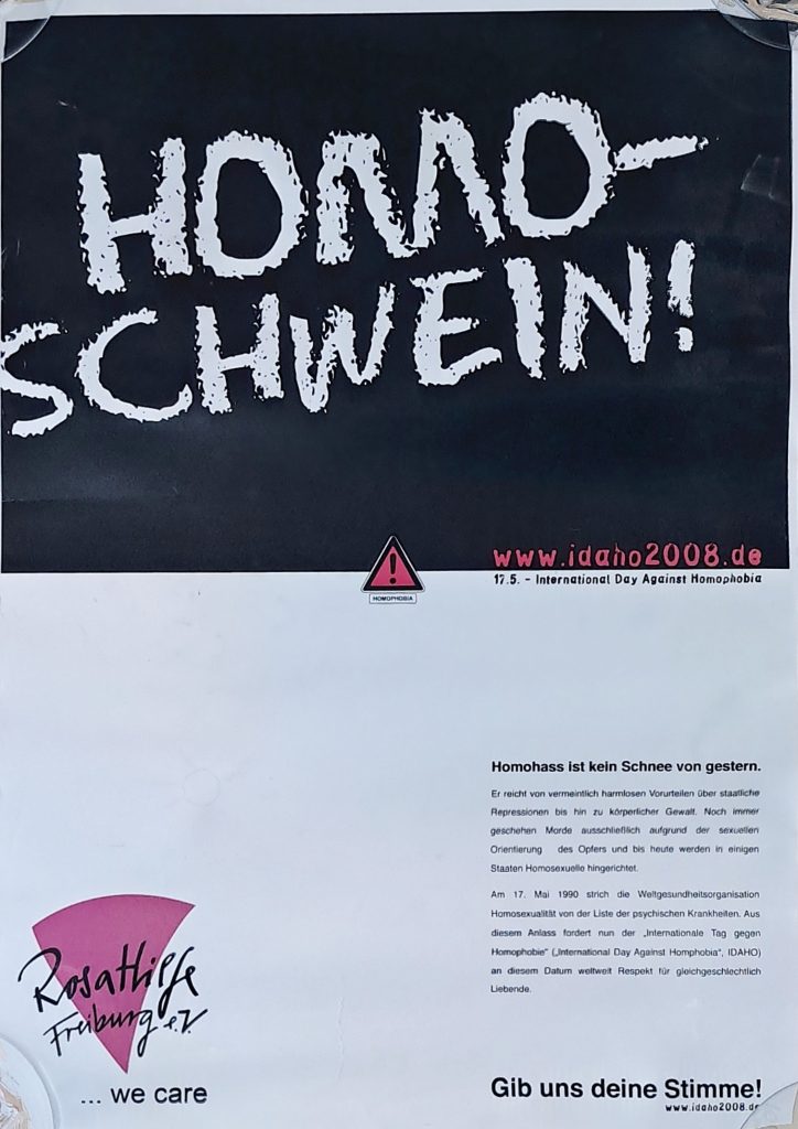 Plakat, zeigt eine Tafel mit Kreideschrift ,,Homoschwein!" und Logo der Rosa Hilfe, Text "Homohass ist kein Schnee von gestern. Er reicht von vermeintlich harmlosen Vorurteilen über staatliche Repressionen bis hin zu körperlicher Gewalt. Noch immer geschehen Morde ausschließlich aufgrund der sexuellen Orientierung des Opfers und bis heute werden in einigen Staaten Homosexuelle hingerichtot. Am 17. Mai 1990 strich die Weltgesundheitsorganisation Homosexualität von der Liste der psychischen Krankheiten. Aus diesem Anlass fordert nun der „Internationale Tag gegen Homophobie“ („International Day Against Homphobia*, IDAHO) an diesem Datum weltweit Respekt für gleichgeschlechtlich Liebende. ... we care Gib uns deine Stimme! www.idaho2008.de"