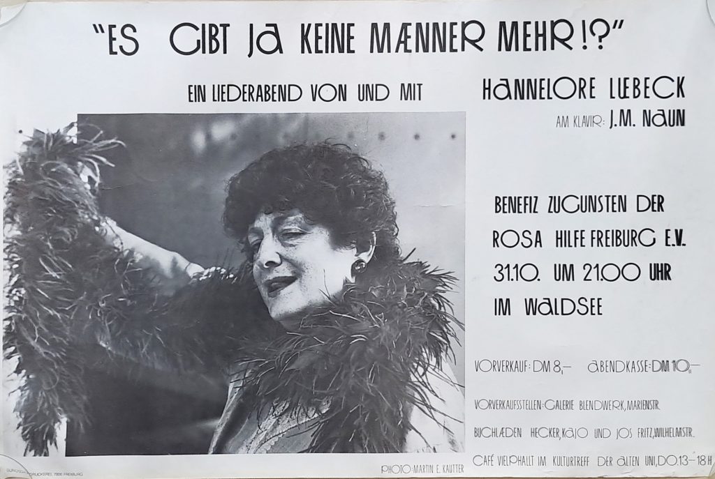 Poster in schwarz weiß mit Photo von H. Lübbeck mit Federboa, stilisierte runde schrift. Text: "ES GIBT Ja KEINE MÄNNER MEHR !? " EIN LIEDERABEND VON UND MIT HANNELORE LUEBECK AM KLAVIR: J.M. NAUN BENEFIZ ZUGUNSTEN DER ROSA HILFE FREIBURG E.V. 31.10. UM 21.00 UHR IM WALDSEE VORVERKAUF: DM 8,- ABENDKASSE: DM 1O- VORVERKAUFSSTELLEN: GALERIE BLENDWERK, MARIENSTR. BUCHLÄDEN HECKER, KaJO UND JOS FRITZ,WILHELMSTR. PHOTO:MARTIN E. KAUTTER CAFÉ VIELPHALLT IM KULTURTREFF DER ALTEN UNI DO.13-18H