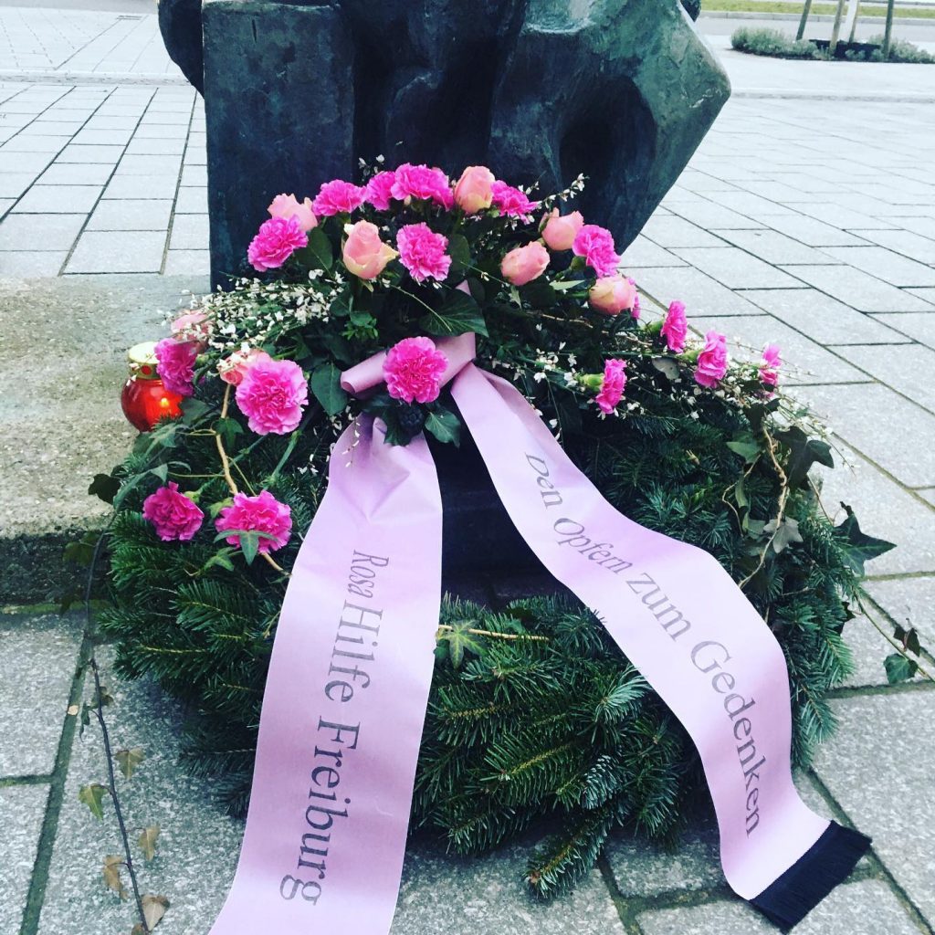 Blumenkranz mit rosa Blüten und Rosa Schriftband vor dem Mahnmal für die Opfer des Faschismus in Freiburg