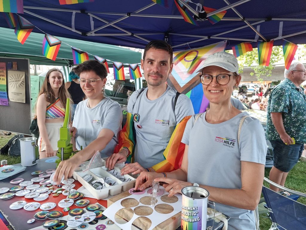 drei Personen in Rosa Hilfe T-Shirts am Infostand, machen Buttons